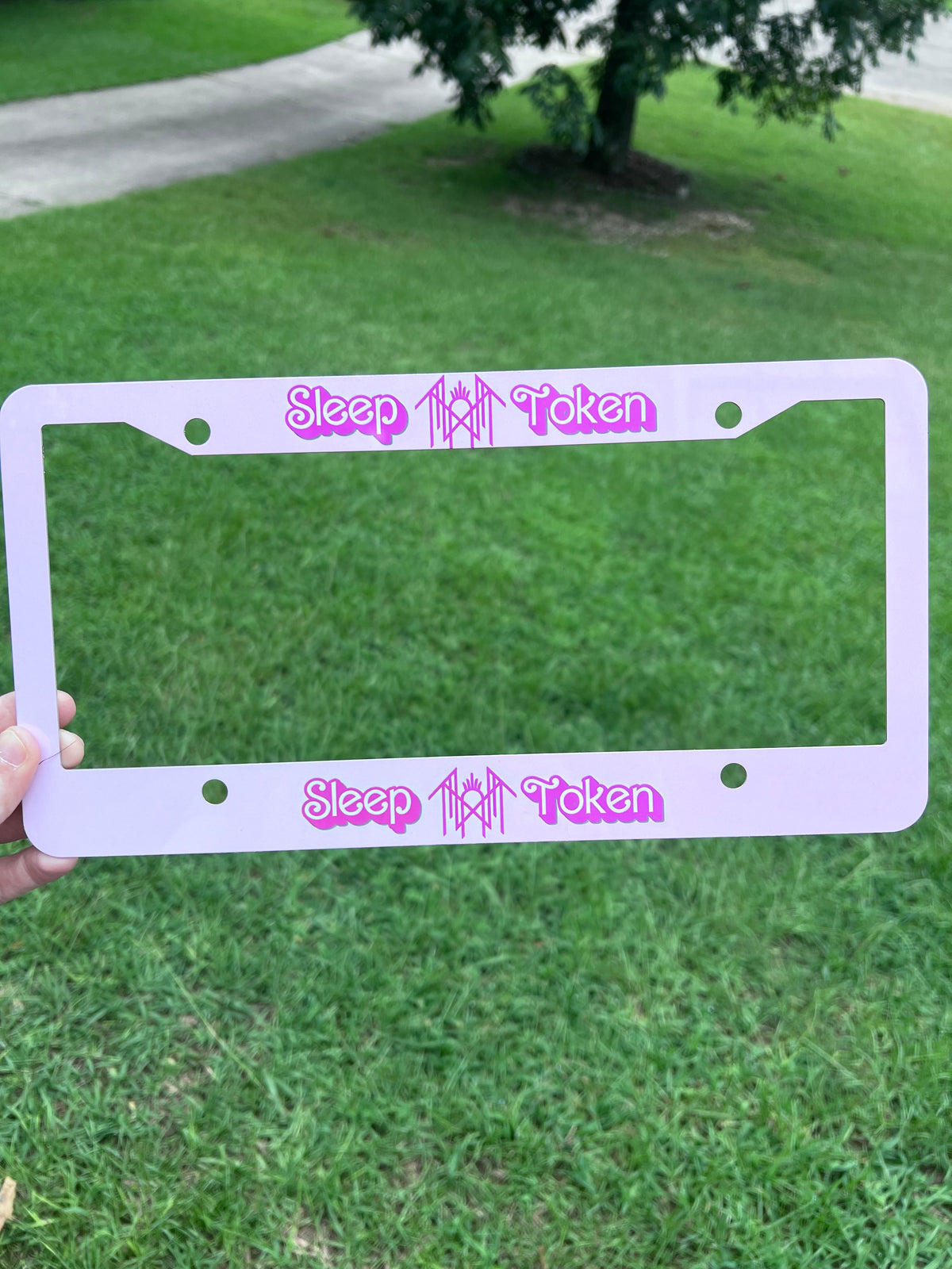 KimTheGrimm Sleep Token Barbie pink sublimated license plate frame held outside in grass background.⁠