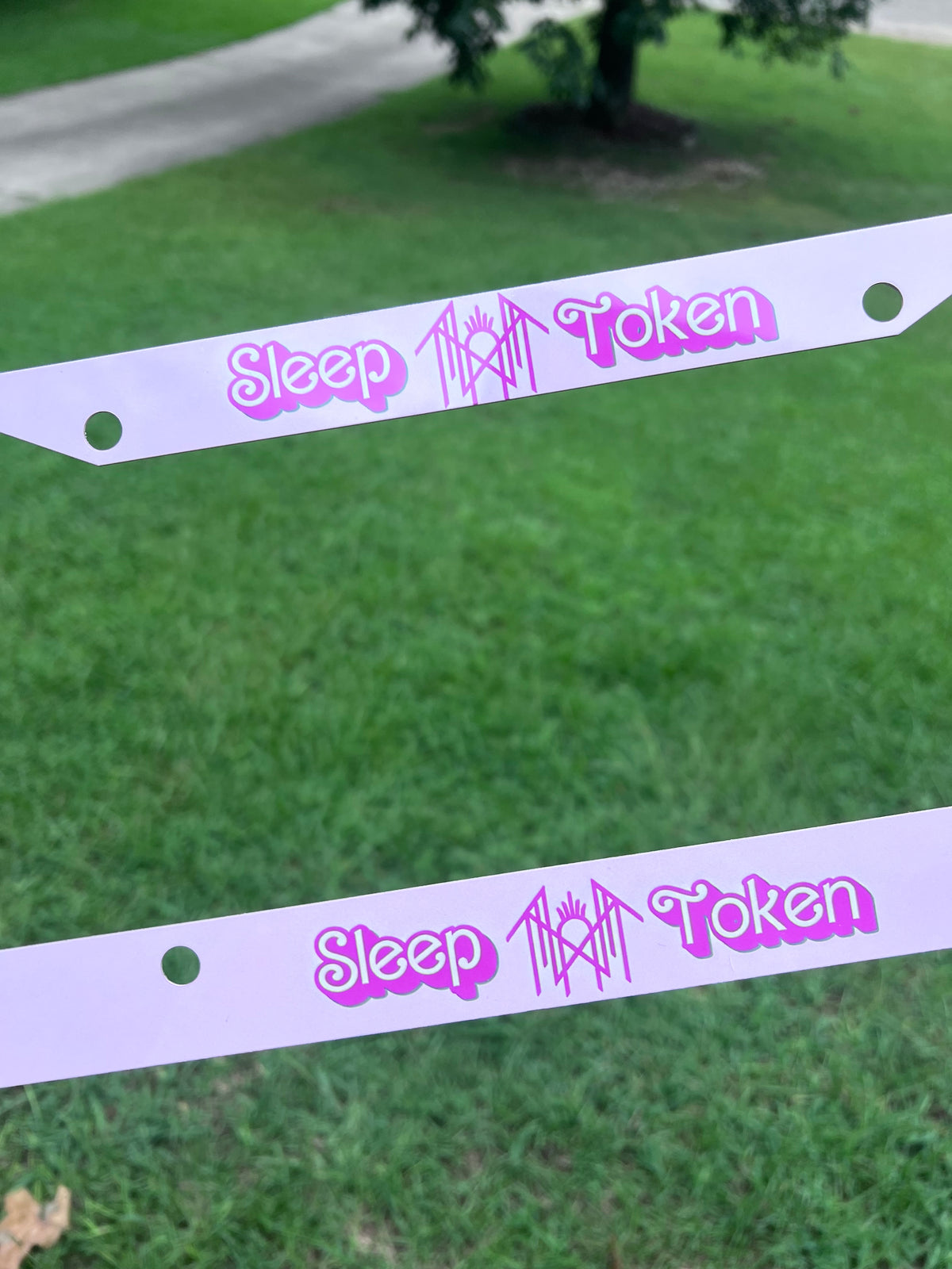 KimTheGrimm Sleep Token Barbie pink sublimated license plate frame held outside in grass background.⁠