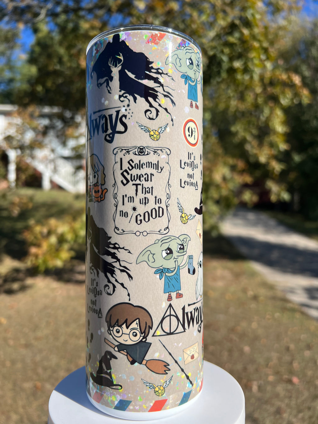 20oz holographic glitter tumbler outdoors featuring Harry Potter chibi characters, Hermione Granger, Hedwig the owl, and the Deathly Hallows Always symbol on a sparkly beige background.