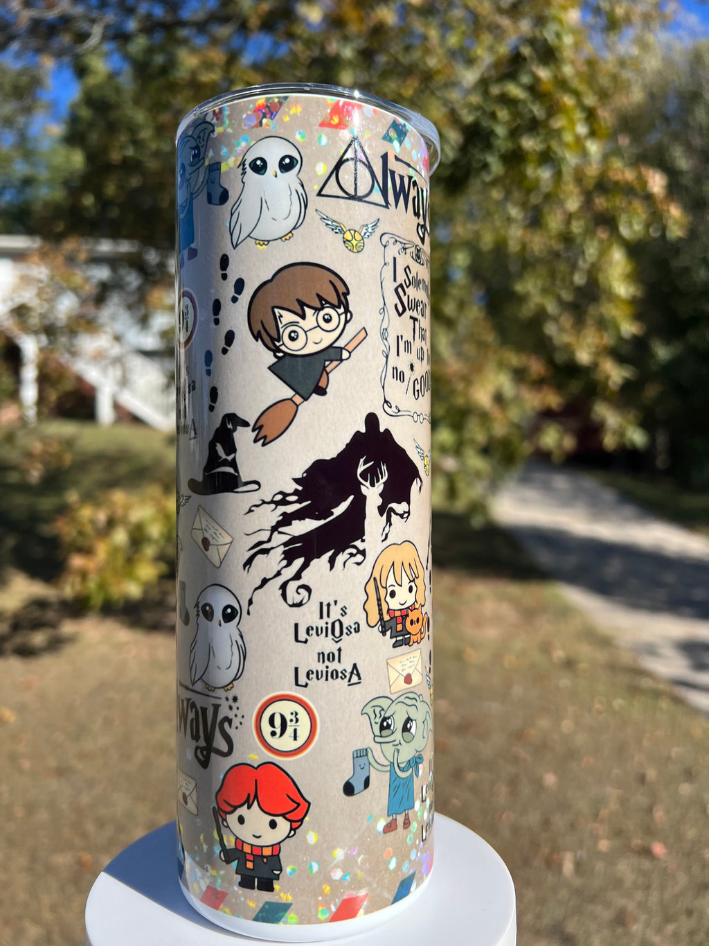 20oz holographic glitter tumbler outdoors featuring Harry Potter chibi characters, Hermione Granger, Hedwig the owl, and the Deathly Hallows Always symbol on a sparkly beige background.