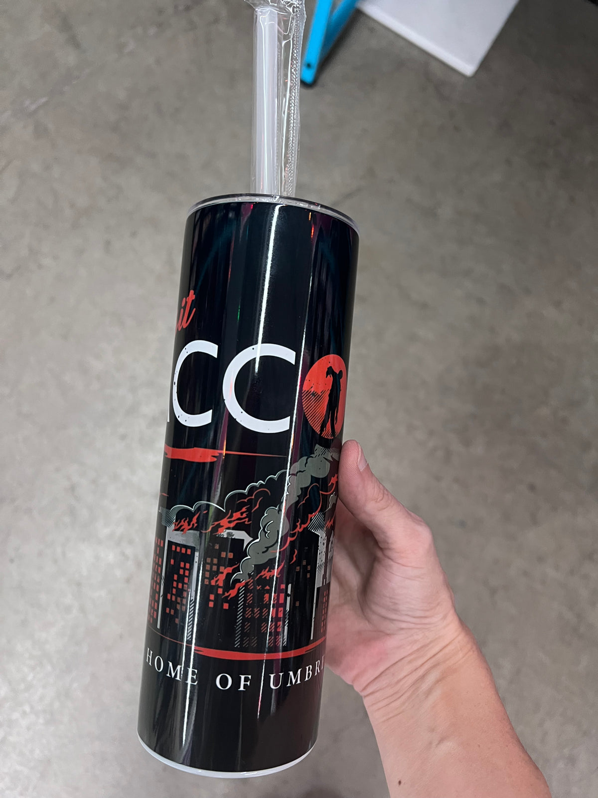 A survival horror themed tumbler displaying a dark city skyline with flames, alongside the text "Visit RACCOON City" with a zombie silhouette inside the lettering