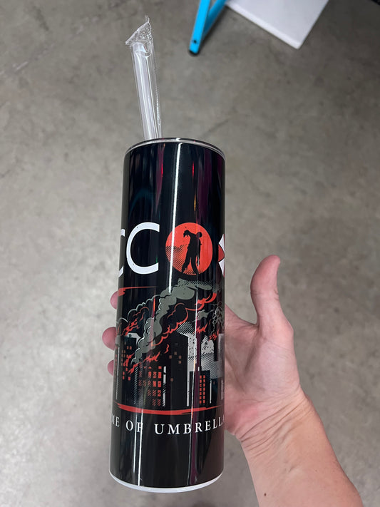 A survival horror themed tumbler displaying a dark city skyline with flames, alongside the text "Visit RACCOON City" with a zombie silhouette inside the lettering