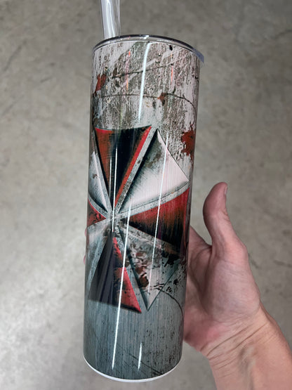A hand holding a custom tumbler featuring the red and white Umbrella Corporation logo set against a heavily distressed, scratched concrete and metal background.