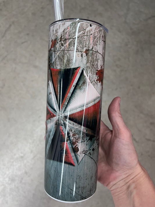 A hand holding a custom tumbler featuring the red and white Umbrella Corporation logo set against a heavily distressed, scratched concrete and metal background.