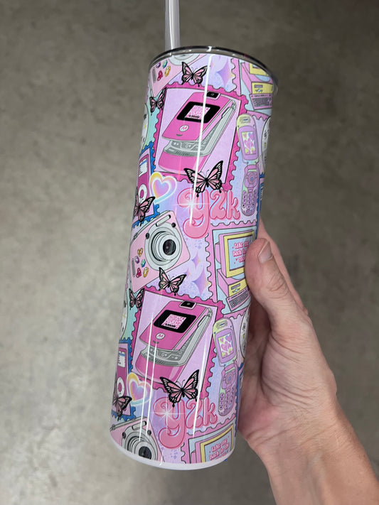 A hand holding a custom sublimated tumbler featuring a pastel Y2K nostalgia design with a pink flip phone, butterflies, and a retro polaroid camera.